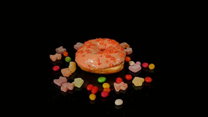 橙色有趣的惊喜釉面甜甜圈，条纹焦糖糖果，彩色糖衣糖衣，里面有葡萄干或花生，在黑色背景上旋转