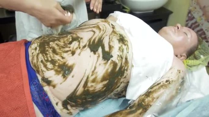 美容师在美容沙龙中推迟了从胖女人肚子上包裹的海藻
