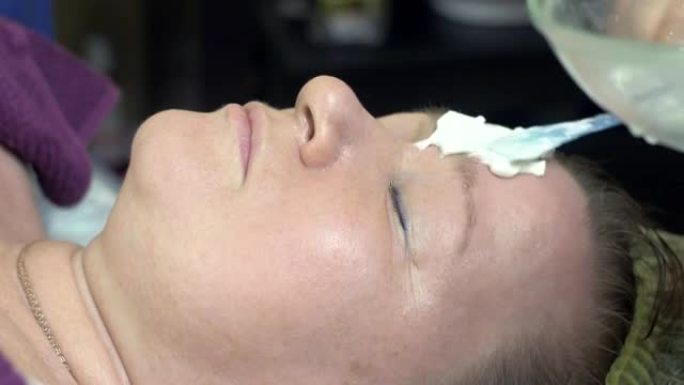 美容师用勺子在美容院的厚女人脸上戴上白色面具