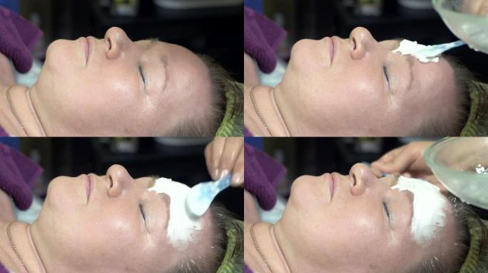 美容师用勺子在美容院的厚女人脸上戴上白色面具