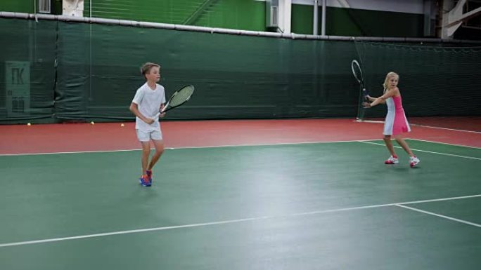 两个快乐的孩子用球拍在球场上发球和还球训练技巧。在娱乐区玩体育游戏的漂亮男孩和女孩。未来的职业球员上
