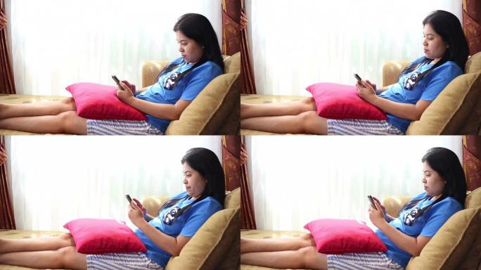 亚洲女人在家里的沙发床上玩智能手机