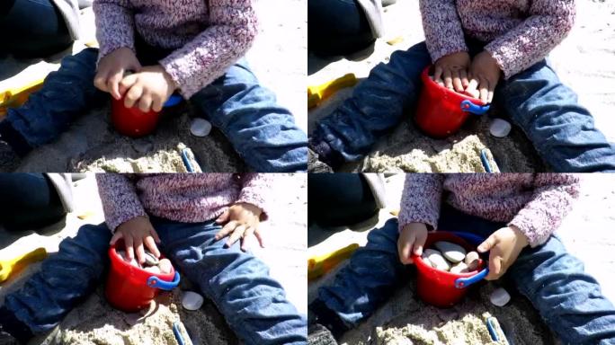 婴儿坐在沙滩上玩水桶里的石头
