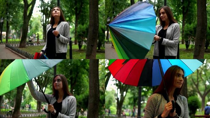 美丽的女人检查是否下雨，然后打开她的彩色雨伞站在城市公园里。慢动作镜头