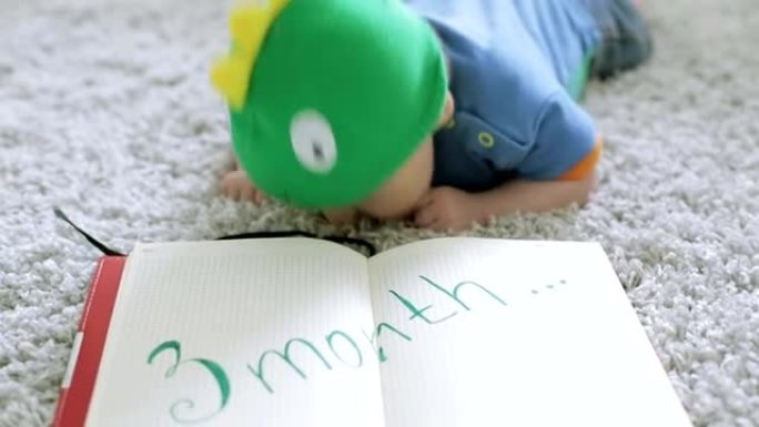 戴着绿龙帽子的三个月婴儿躺在地板上的笔记本上。