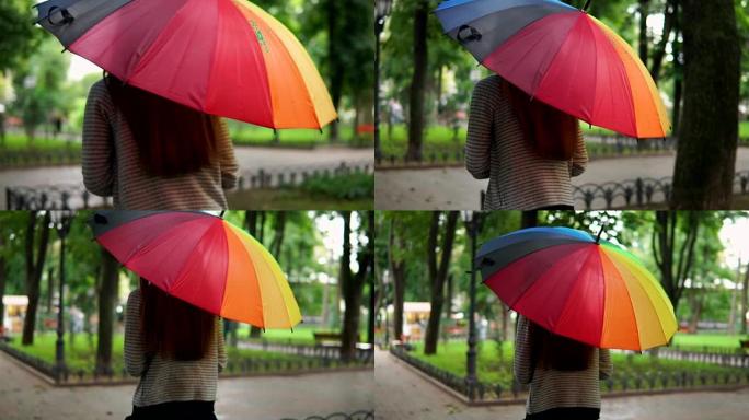 在城市公园里，一个面目全非的女人在雨中打着五颜六色的雨伞奔跑。慢动作镜头