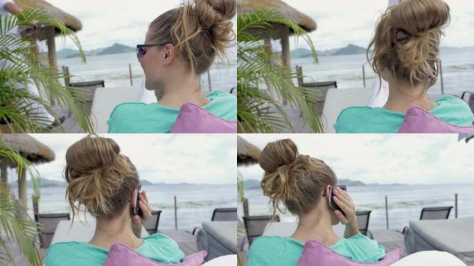 女人坐在海边的躺椅上，使用智能手机。