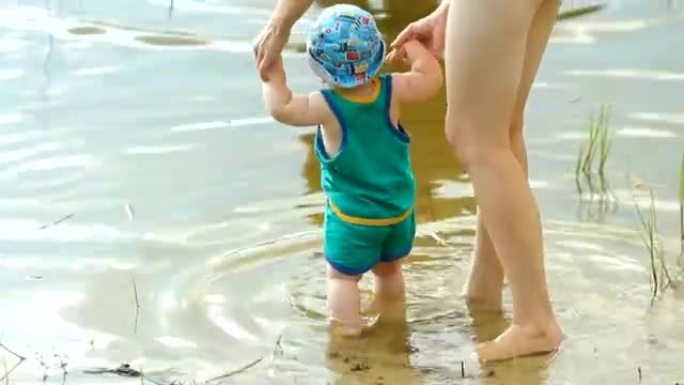 母亲和祖父在湖里和男婴玩耍。漂亮的孩子在水上行走