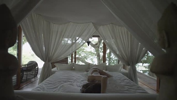 熟睡的女孩醒了。天篷下的浪漫床。森林里的卧室。女人伸懒腰，打哈欠，在床上醒来。醒来，迅速起床。睡过头
