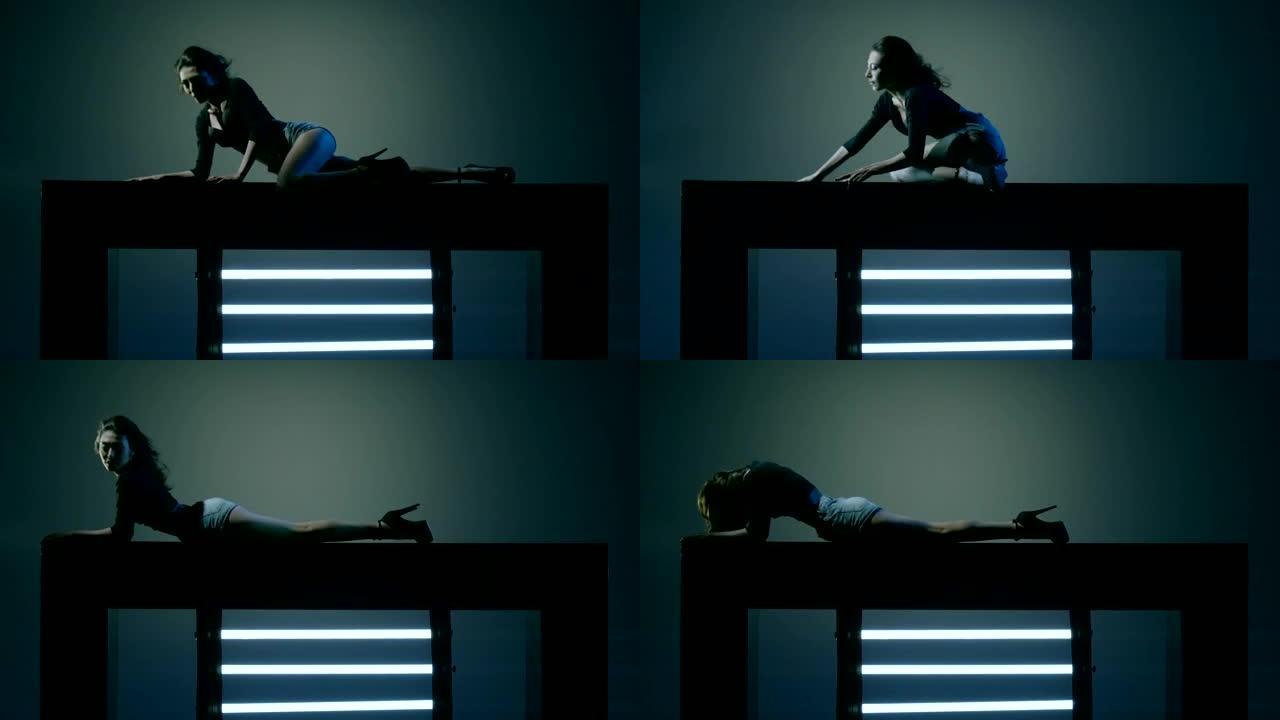 性感的黑发在蓝色深色背景上跳舞。美丽的女孩跳舞，躺在立方体上。在慢动作的红色史诗巨龙电影相机上拍摄。