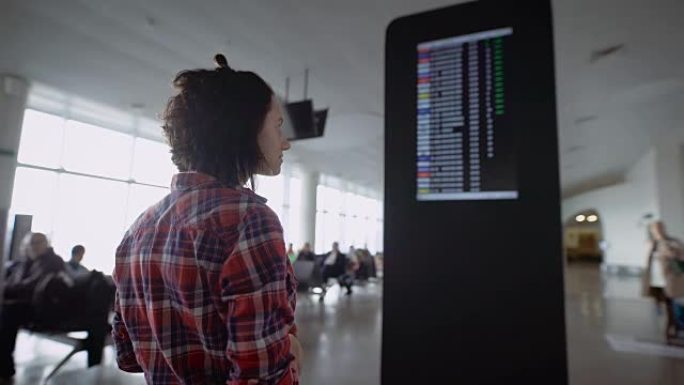 女孩站在机场，期待着关于降落在飞机上的广告。布鲁内特考虑计分板和飞机时间表，看着他的手表，用她的智能