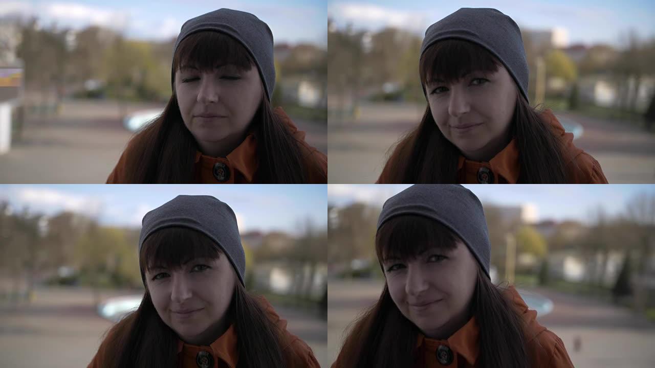 年轻迷人的黑发刘海女孩，棕色眼睛，戴着灰色帽子和橙色夹克，站在街上，看起来笔直而悲伤的微笑