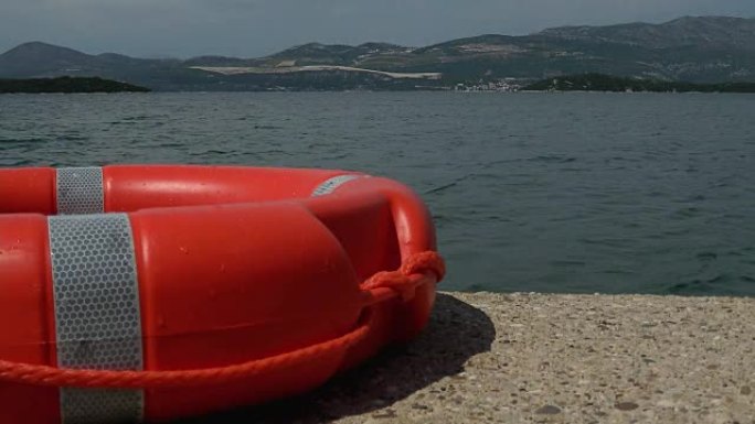 特写镜头的红色救援浮标靠在码头上，海水漂浮在背景中