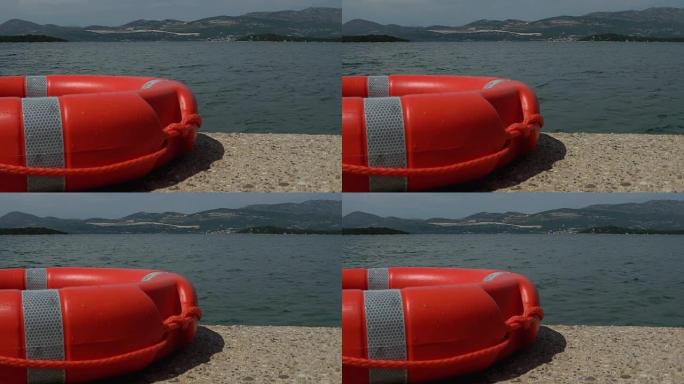 特写镜头的红色救援浮标靠在码头上，海水漂浮在背景中