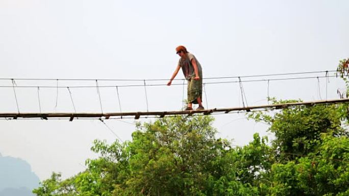 老挝穿越危险竹吊桥的旅游妇女