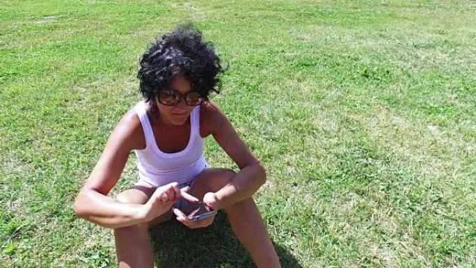 戴眼镜的哈皮女性使用智能手机坐在草地上冲浪，4k steadicam