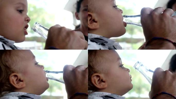 婴儿用玻璃瓶喝水。父母帮助婴儿从奶瓶中喝水