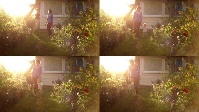 一位年轻的母亲带着一个年幼的儿子在日落时离开家在花园里散步