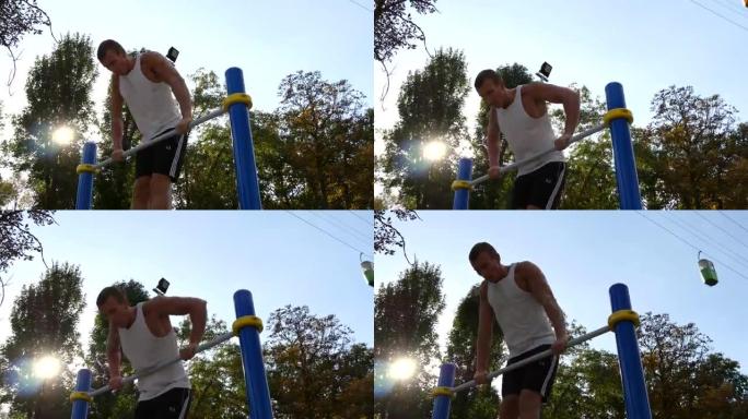 强壮的肌肉男人在公园里做肌肉锻炼。年轻运动员在室外单杠上做俯卧撑。健身肌肉男夏天在外面训练。运动员停