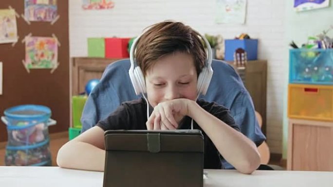 可爱的小男孩使用数字平板电脑观看有趣的视频，戴着耳机