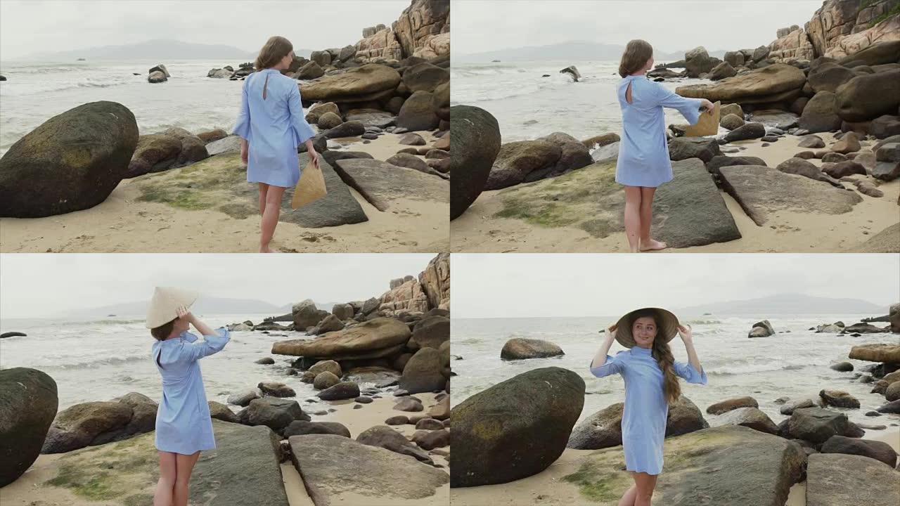 一个穿着蓝色礼服的女孩沿着海边散步，戴上越南帽子，微笑着