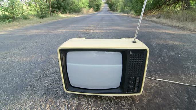 空旷的乡村道路上带有闪烁屏幕的老式电视