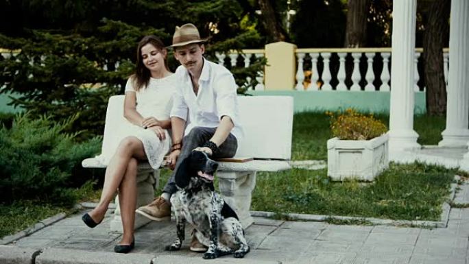 年轻的男人和女人坐在长凳上，男人抚摸着狗