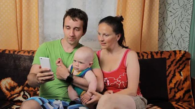 妈妈，小宝贝和爸爸在电话里做视频交流。一家人坐在家里的沙发上微笑着