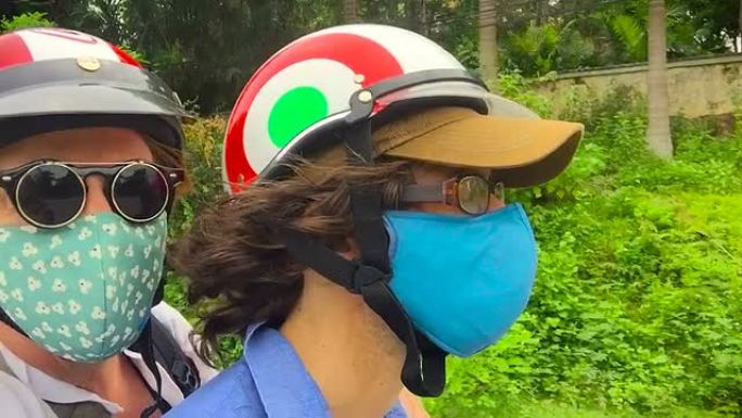 在热带地区，两个人骑着戴着口罩和头盔的踏板车的特写镜头