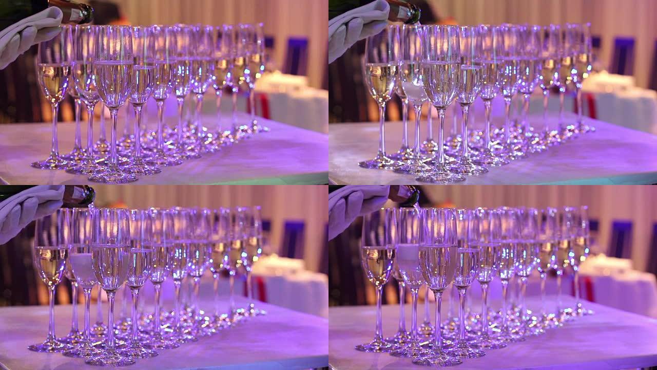 服务员将香槟倒入酒杯，自助餐桌上的香槟杯，餐厅或酒店的大厅，服务员的手戴着白手套，一瓶香槟，室内，特