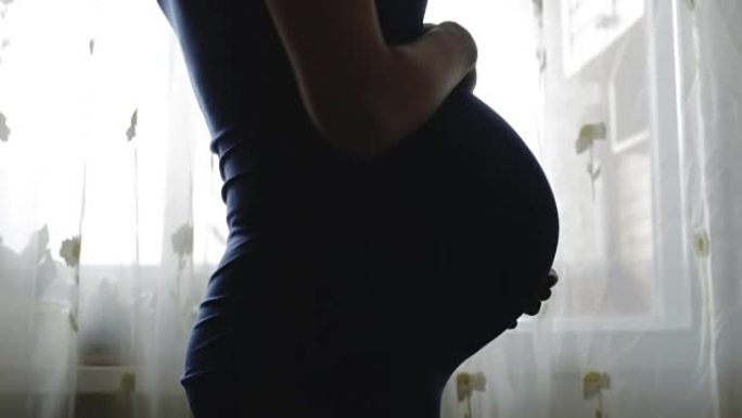 一名孕妇站在窗前，侧身转身。
