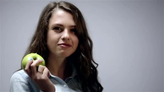 年轻女子在灰色背景下吃青苹果