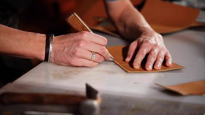 一个男人的手的特写镜头，用刀在皮革细节上做一个笔记
