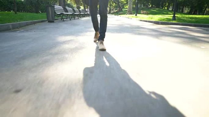 移动摄像机拍摄的脚和早晨一个人在公园小巷上行走的阴影