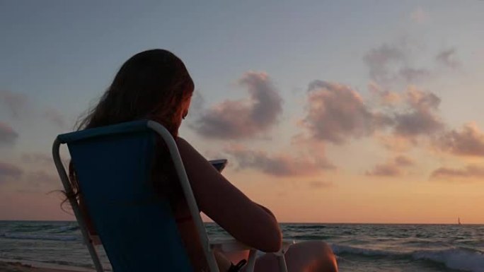 带智能手机的年轻女孩在特拉维夫海滩的美丽日落。