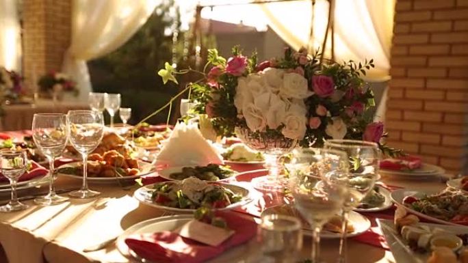 婚礼桌乡村风格的装饰，配有粉色和米色的菜肴、饮料和鲜花。派对宴会餐桌上玫瑰的植物组合
