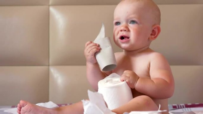迷人的婴儿坐在床上撕开卫生纸。孩子1年