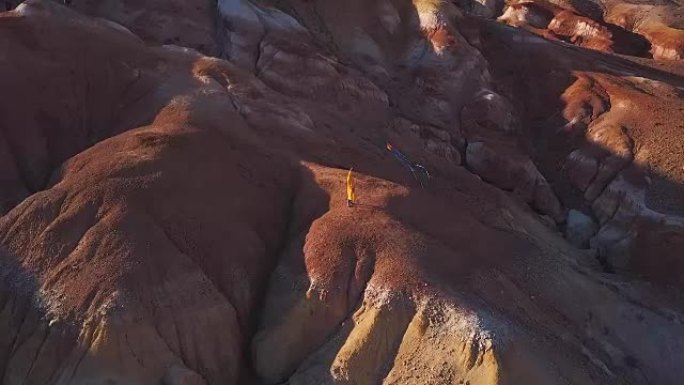 空中: 一个年轻的女孩站在红山上放风筝在高山上的背景。自由的想法，在山里寻找冒险。这个女孩梦想一个更