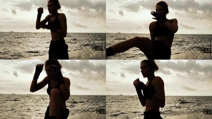 女拳击手使她的腿对着太阳的海边在慢动作侧踢。美丽的女拳击手早上在沙滩上训练，拳打脚踢