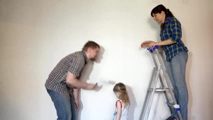妈妈，爸爸，女儿的家人用画笔和滚筒涂漆墙。