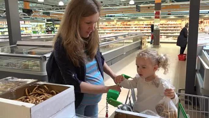 怀孕的母亲和可爱的女孩在购物市场上挑选百吉饼饼干