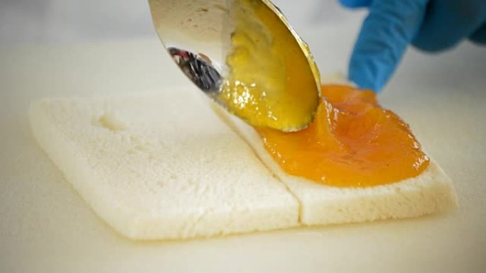 厨师用勺子在一片面包上涂抹果酱桃子