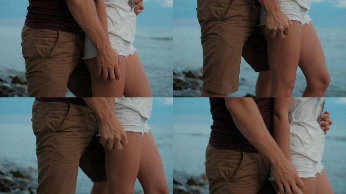 男人热情的手在岩石海滩上挤压穿着短裤的女人