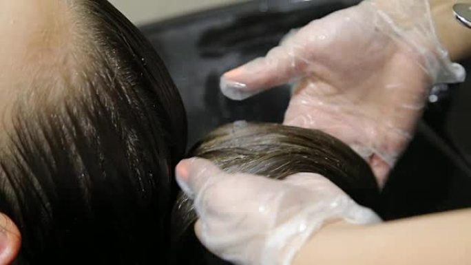 穿着手套的理发师在沙龙洗年轻女子的头发