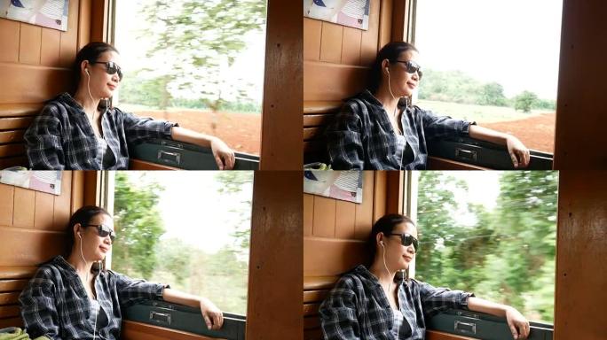 4K。美丽的亚洲女人戴着太阳镜，从火车窗外看耳机听音乐。享受在泰国，亚洲各地乘坐老式火车的交通。休闲