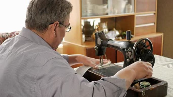 一个留着小胡子的成年男子在一台旧手工缝制的机器上缝制。戴眼镜，缝白布