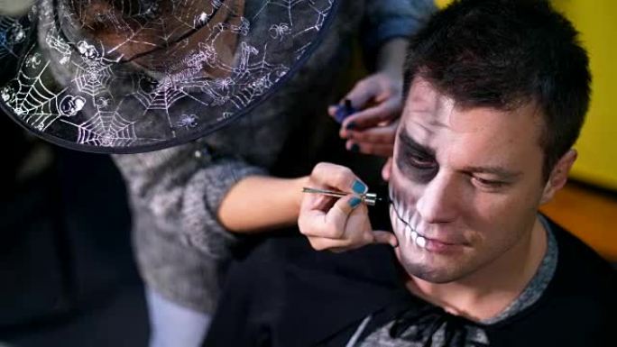 万圣节派对，特写，化妆师为万圣节派对在一个男人的脸上画了一个可怕的妆容。在背景中可以看到万圣节风格的
