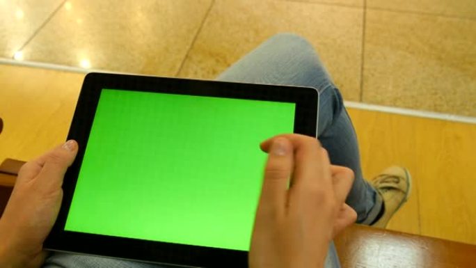 年轻女孩坐在购物中心的长凳上，用平板电脑工作。女性双手使用绿屏平板电脑。色度键