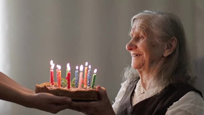 满头白发的快乐老妇人在蛋糕上吹蜡烛。
