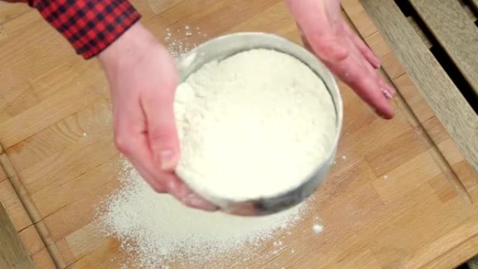 厨师用筛子筛面粉。在木板上准备面团。小麦粉。